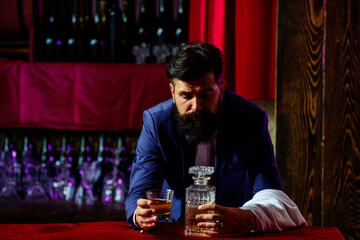 Handsome bearded barman with long beard and mustache with serious face made alcoholic cocktail in vintage suit on red bar background.