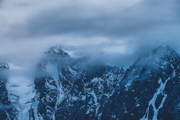 Plakat Mysterious dramatic alpine scenery with snowy mountain top inside low clouds in dusk. Bleak view to glacier in cloudy sky in twilight. Atmospheric minimalist landscape with snowy rocks in dense fog.