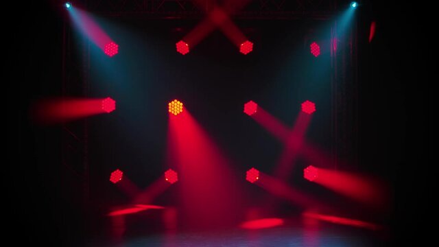 Red moving spotlights and blue beams on an empty stage in the dark. Stage lighting. Dynamic light show. Lights shining on disco party, wedding or birthday celebration, or at nightclub entertainment.