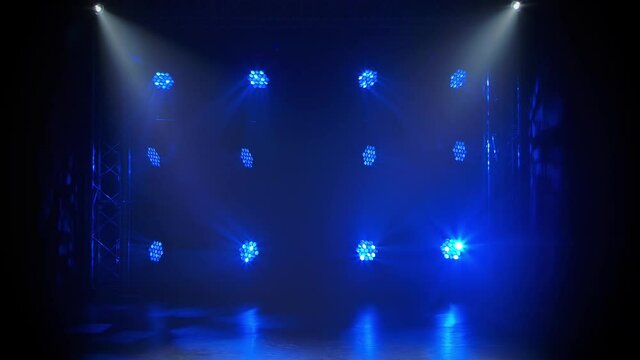 Blue moving light and white rays on an empty stage in the dark. Stage lighting. Dynamic light show. The lights are shining on disco party, wedding or birthday celebration or at nightclub entertainment