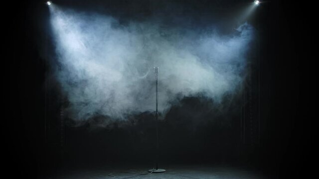A vintage metal microphone looms against a black studio background of smoke. The smoke dissipates and a microphone appears shining in the studio light.