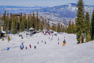 View of Colorado ski resort in winter: people skiing and snowboarding to base of chairlift; forest...