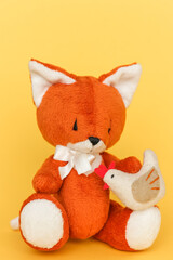 Soft toy ginger fox with chicken on a yellow background.