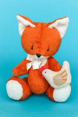 Soft toy ginger fox with chicken on a blue background.