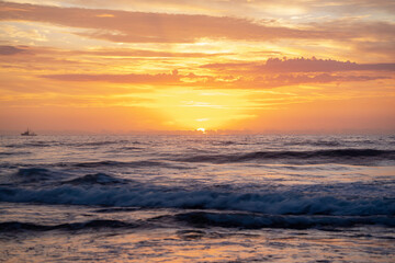 Fototapeta na wymiar Sunrise over the beach with silhouette of boat on the horizon