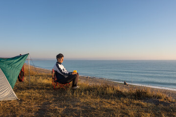 Adult woman by the sea drinking coffee in front of the tent