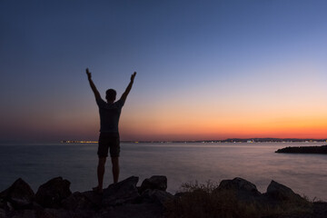 Silhouette of a man greeting the sunset by the sea