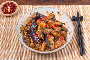 Korean spicy eggplant with spicy sauce and sesame seeds in a large bowl and chopsticks on a bamboo napkin on a rustic wooden table