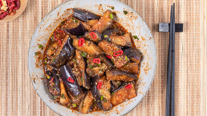 Korean spicy eggplant with spicy sauce and sesame seeds in a large bowl and chopsticks on a bamboo napkin on a rustic wooden table, top view