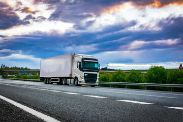 Refrigerated semi-trailer truck driving on a highway under a dramatic sunset sky.