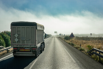 Tipper truck driving down the straight of a highway with a bank of fog in the background.