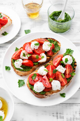 Bruschetta with cherry tomatoes, mozzarella cheese and pesto sauce on wooden board. Traditional italian appetizer or snack, antipasto.	