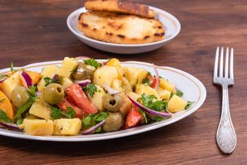Traditional Italian Calabrian potato salad - oval plate with boiled potatoes, tomatoes, onions and olives on a plain table close-up
