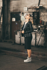 Fototapeta na wymiar Blonde girl wearing leather jacket and a stretched mini dress in an old spooky factory