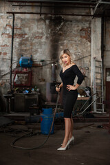 Fototapeta na wymiar Blonde woman wearing black dress holding a welding torch in an old spooky factory