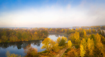 Fototapeta na wymiar Autumn landscape: The river is surrounded by yellow trees in the fog in November. Warm calm panorama of autumn. 