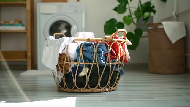 Basket of dirty clothes is standing on floor in laundry room at home spbd. Close-up view of container filled with clothing stands on background of washing machine indoors. Picture of house during