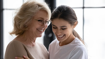 Wide panoramic view of overjoyed elderly mom and grownup daughter embrace enjoy happy tender family moment together. Smiling mature mother and grateful adult girl child hug show love and care.