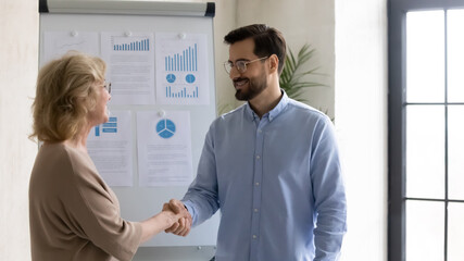 Smiling businessman shake hand of middle-aged female employee greeting with job success or...