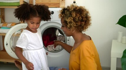 afro mom and daughter load washer with dirty clothes Spbd. mother and kid do housework with washing machine. child help mom with laundry and housework. concept domestic, american, bathroom - Powered by Adobe