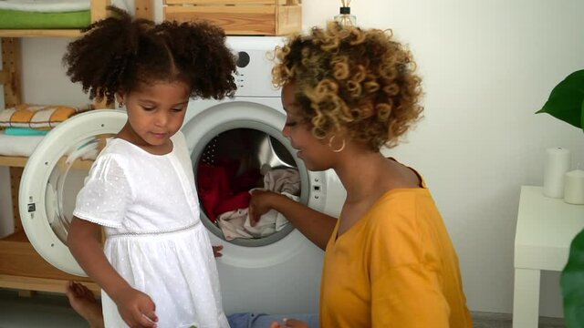 Afro Mom And Daughter Load Washer With Dirty Clothes Spbd. Mother And Kid Do Housework With Washing Machine. Child Help Mom With Laundry And Housework. Concept Domestic, American, Bathroom