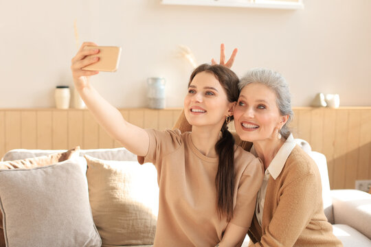 Happy middle aged mother and daughter taking selfie at home.