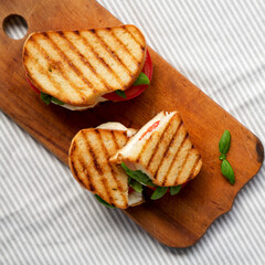 Tasty Grilled Caprese Panini (Mozzarella, Tomatoes and Basil) on a rustic wooden board, top view. Flat lay, overhead, from above. Close-up.