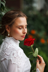 Fototapeta na wymiar beautiful girl in a vintage dress walks in the garden, bride with a red rose in her hands