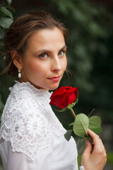 beautiful girl in a vintage dress walks in the garden, bride with a red rose in her hands