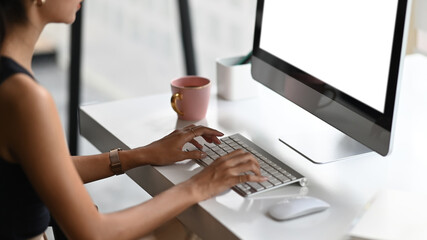 Cropped shot of professional designer typing on blank screen computer in minimal workspace on white table.