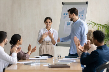 Businessman introduce excited ethnic female worker or employee to team at group office meeting. Diverse businesspeople greeting congratulating happy woman colleague with job success or promotion.
