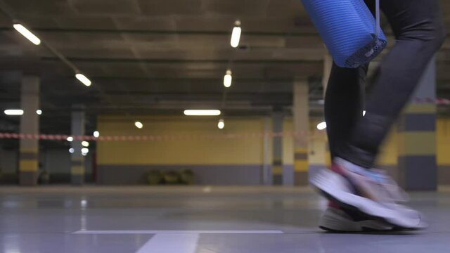 Teenager sport girl walking inside parking garage. Woman holding yoga mat. Urban city lifestyle outdoors concept. Close up of her feet