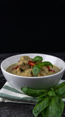 Traditional Thai cuisine, green curry chicken in white bowl over dark background