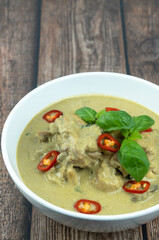 Traditional Thai cuisine, green curry chicken in white bowl over wooden background