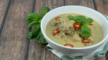 Traditional Thai cuisine, green curry chicken in white bowl over wooden background