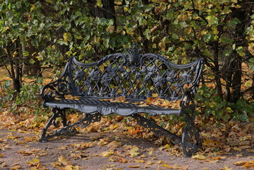 Yellow leaves, autumn day and black cast bench in autumn Park