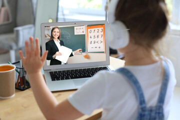 Distance learning. Cheerful little girl using laptop computer studying through online e-learning...
