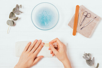Woman cares for her cuticles with moisturizing oil next to set of manicure tools