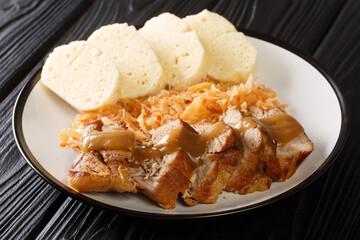 Roasted pork with stewed sauerkraut and dumplings close-up in a plate on the table. horizontal