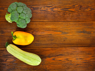 Fresh broccoli with zucchini and yellow sweet pepper on a wooden background. Text space. Top view.