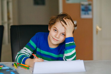 Portrait of cute happy school kid boy at home making homework. Little child writing with colorful pencils, indoors. Elementary school and education. Kid learning writing letters and numbers