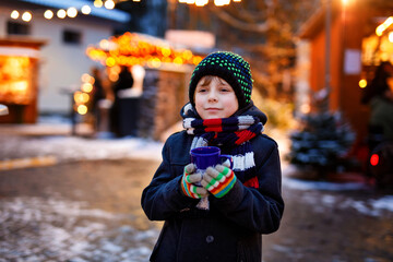 Little cute kid boy drinking hot children punch or chocolate on German Christmas market. Happy...