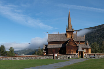 Fototapeta na wymiar Stave Church of Lom in Norway with blue sky and clouds hanging low