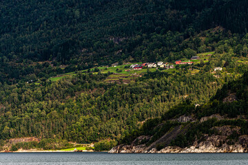traditional farm houses on a steep mountain side in norway with trees, beautiful lighted by the sub...