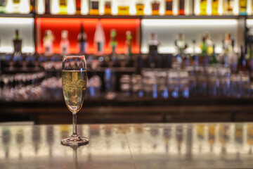 A glass of wine or champagne put on table bar in night club or pub with blur many bottle of alcohol drink background 