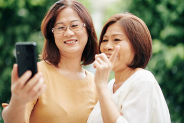 Asian senior women video calling their friend when standing outdoors