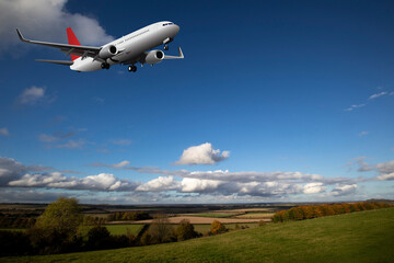 Commercial passenger airplane flying over farmland in rural Hampshire set against blue cloudy sky