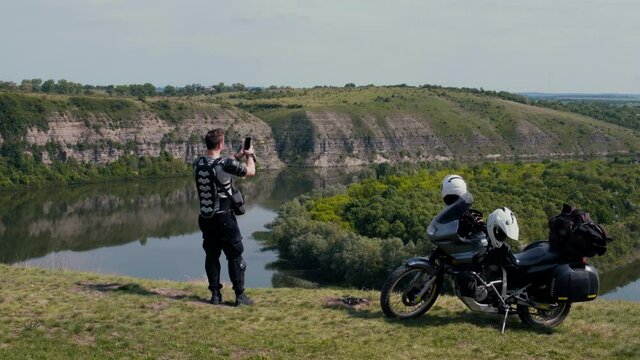 A man biker take a selfie, picture on smartphone. Motorcycle for journeys, extreme lifestyle, tourism and vacation, dark colors. Canyon with the river. Dniester Ukraine