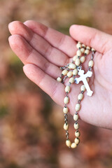 Women's hands holding rosary at the autumn background.