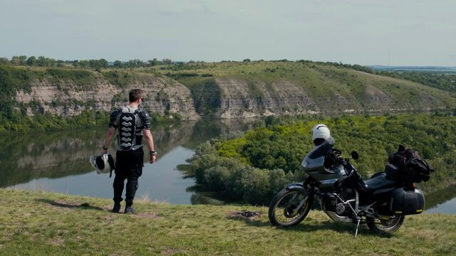 A man enjoy view, take a selfie, picture on smartphone. Motorcycle for journeys, extreme lifestyle, tourism and vacation, dark colors. Canyon with the river. Dniester Ukraine